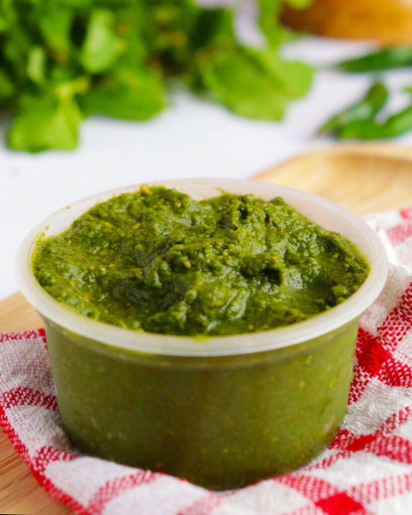 Mint and Coriander Green Chutney in a bowl over a red and white kitchen napkin with herbs in background