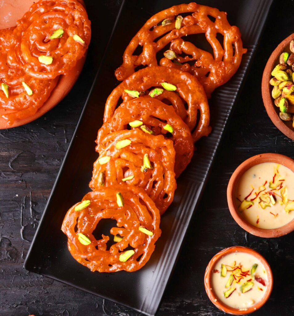 Jalebis on a black tray over a black table with kesar rabri on the side