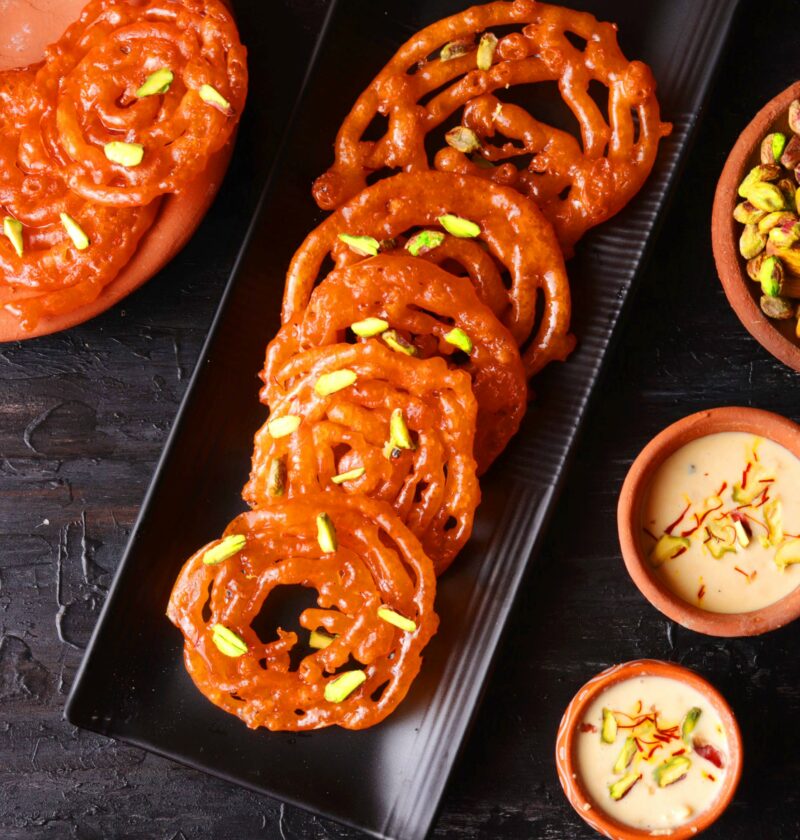 Jalebis on a black tray over a black table with kesar rabri on the side