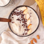 Vegan Sugar-free Banana Nice Cream on a white surface garnished with cacao nibs and almonds