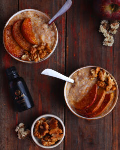 Apple Cinnamon Breakfast Porridge served in a white bowl on a wooden table with an Ossoro sweet apple flavour bottle