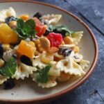 Fruit and nut Pasta Salad on a white cermaic plate over a blue table
