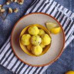 Lemon Truffles in a bowl and white plate on a blue backdrop along will small white flowers