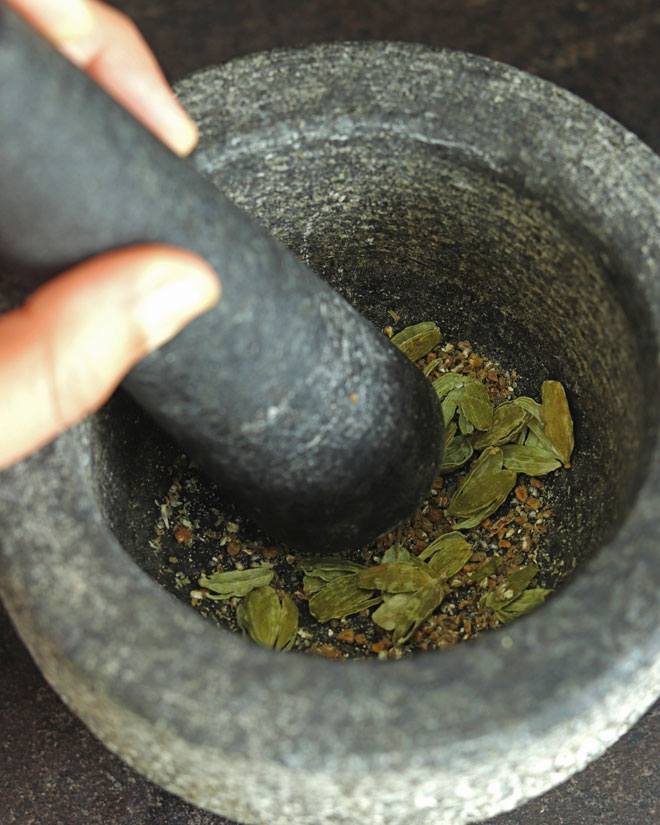 Crushing cardamom pods in a mortar and pestle to make Peanut Sweet Rice with coconut