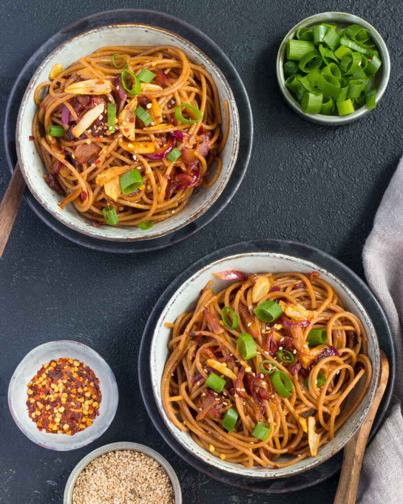 Two bowls of Chilli Garlic Noodles in a white ceramic bowl on a black textured table