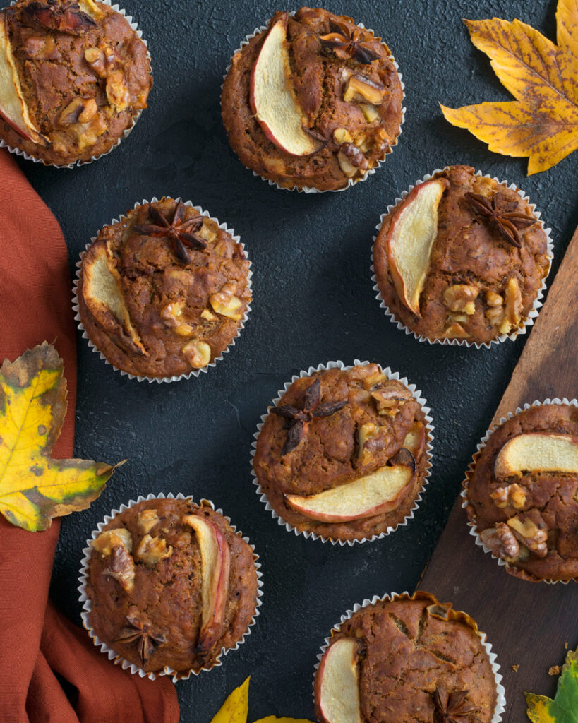Eggless Apple Muffins over a black table with autumn leaves around them and a orange napkin