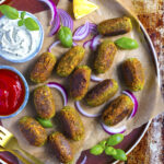 Vegan Matar Kebabs on a copper coloured plate with red onion on the side of ketchup and mayo