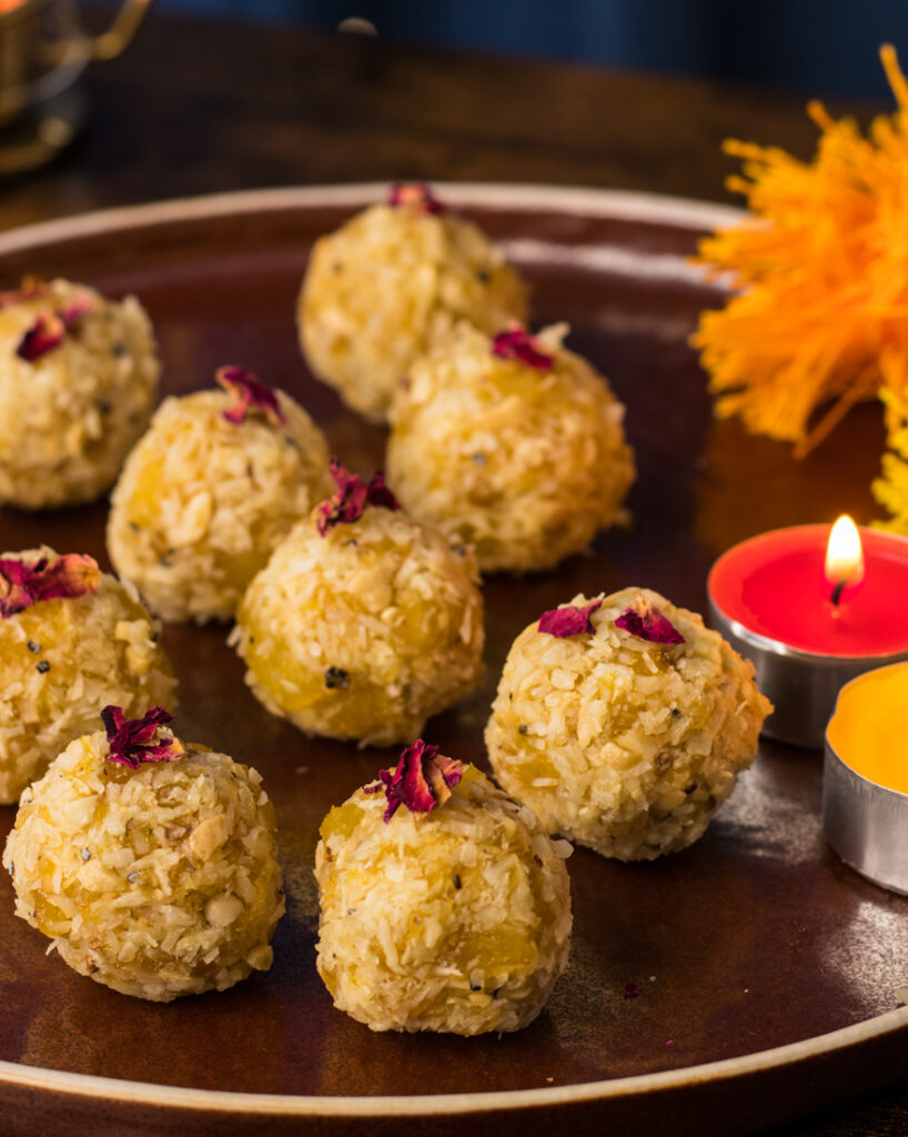 Vegan Pineaaple laddus on a copper coloured plate with yellow and red candles abd flowers